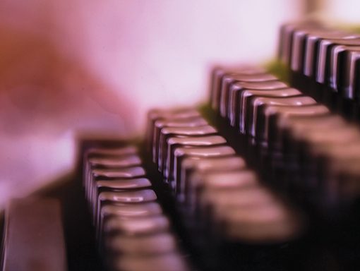 Close-up of blurred vintage typewriter keys, highlighting rows of metallic buttons in soft focus.