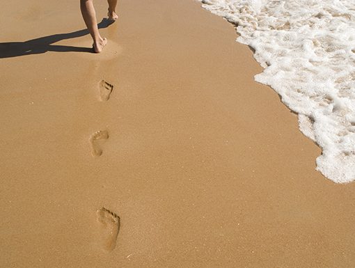 Footprints in the sand near ocean waves, illustrating a relaxing beach walk.