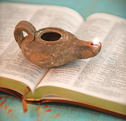 Ancient oil lamp burning on an open book, symbolizing wisdom and knowledge through history and literature.