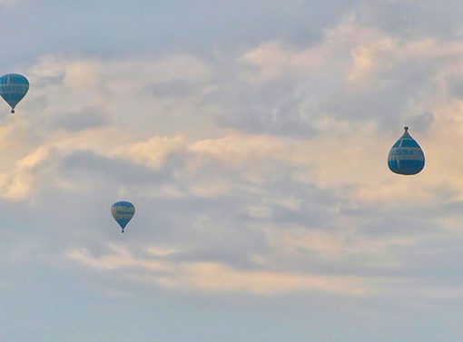 Three hot air balloons float against a cloudy sky, showcasing a serene aerial view.