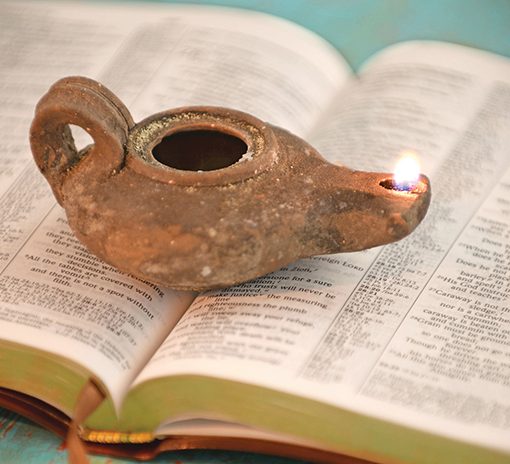 Ancient oil lamp lit atop an open Bible, symbolizing light and wisdom in spirituality and history.
