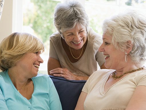 Elderly women laughing and chatting together in a cozy living room setting, showcasing friendship and joy.