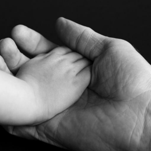 Adult hand holding a child's hand, symbolizing care and support. Black and white close-up image.