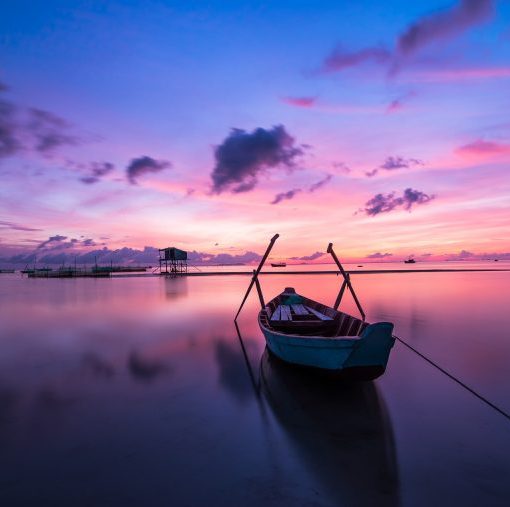 Boat on tranquil water at sunrise with vibrant pink and blue sky, reflecting serene scenery and peaceful atmosphere.
