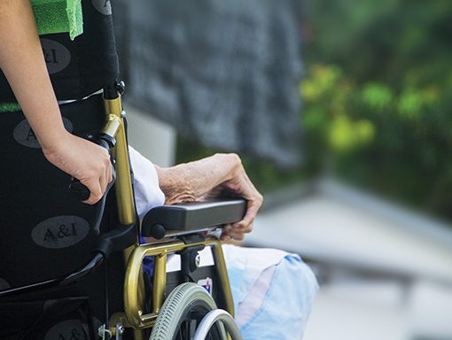 Person in wheelchair with caregiver outdoors, highlighting support and compassion in assisted living environments.