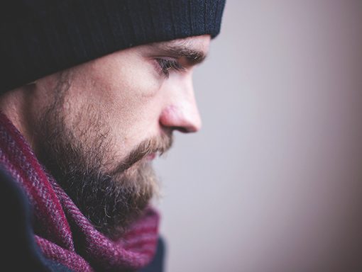 Man in a black beanie and maroon scarf, side profile with a contemplative expression.