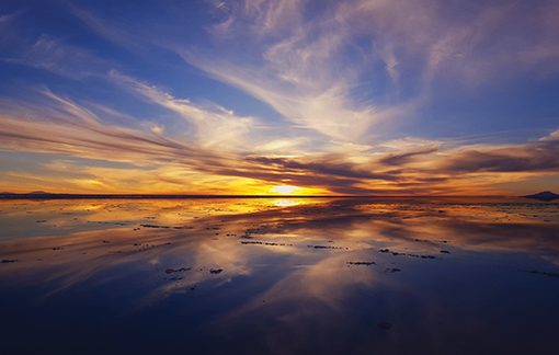Vibrant sunset reflecting on a tranquil lake with dramatic clouds in the sky.