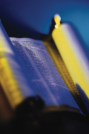Open scroll with text in low light, reflecting a mix of blue and yellow hues, conveying a sense of historical depth.