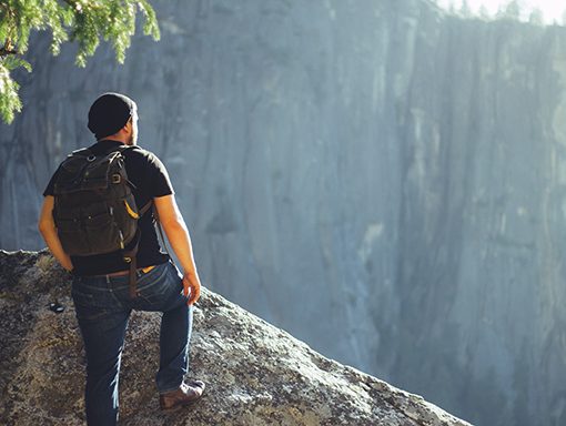 Man with backpack standing on rocky cliff, overlooking a vast natural landscape. Adventure and exploration concept.