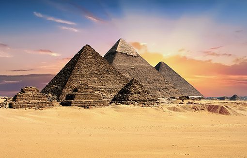 The pyramids of Giza at sunset with a vibrant sky in the background, located in the Egyptian desert.