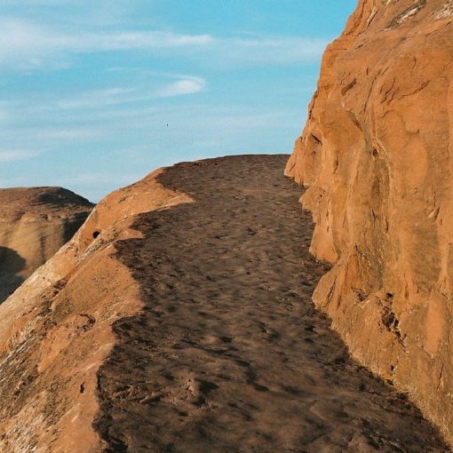 Narrow dirt path along a rocky cliff with clear blue sky in the background.