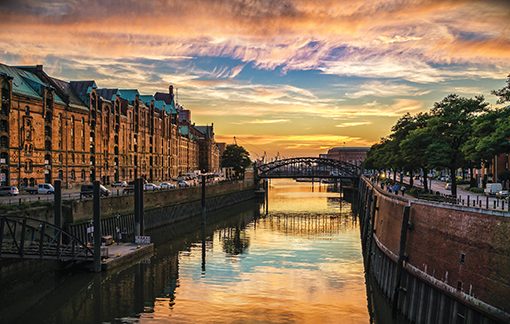 Sunset over a historic canal with old brick buildings and a bridge reflecting in the water.