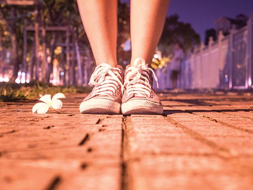 Sneakers on sidewalk next to flower in evening light, signifying a peaceful urban stroll.