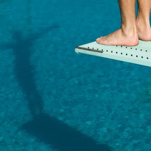 Foot poised on diving board above clear pool water.