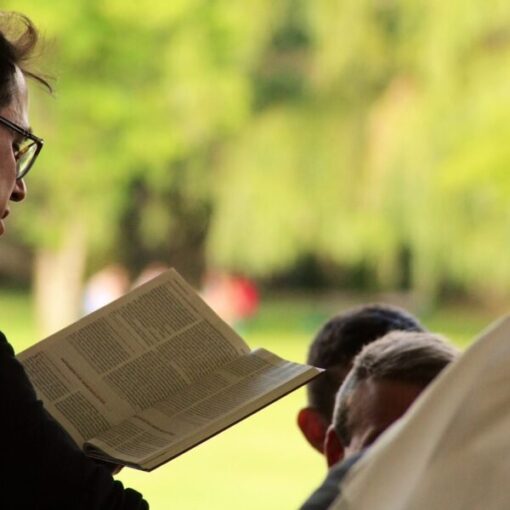 Person reading a book outdoors, surrounded by greenery, creating a peaceful and thoughtful atmosphere.