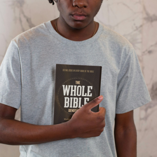 Person holding a book titled The Whole Bible Devotional against a marble background.