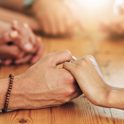 Hands holding on a wooden table, symbolizing support and connection in a warm, sunlit setting.